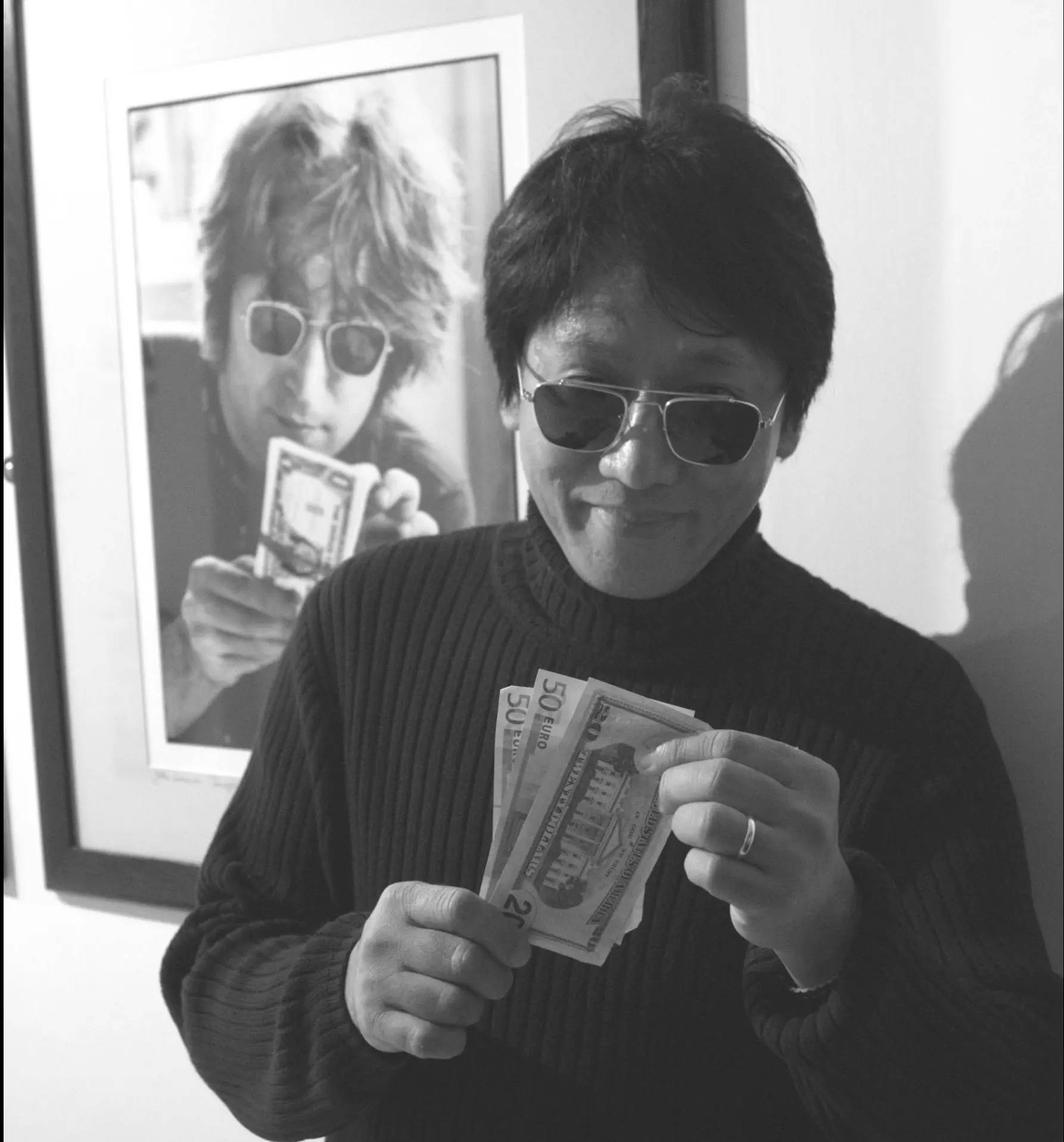 Black and white portrait of musician Resty Garcia in front of a framed John Lennon photograph